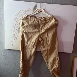 Beiga byxor med snörning från Name It - Snygga beiga byxor från Name It i storlek 152. De har elastisk midja med snörning, sidfickor och en bakficka med liten patch. Perfekta för en chill och avslappnad stil. Materialet känns mjukt och bekvämt, passar till det mesta.