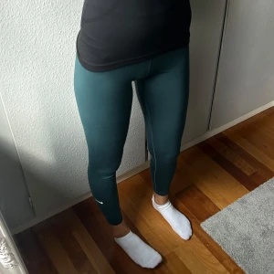 Mörkgröna tights Nike - Säljer ett par mörkgröna tights med hög midja och tight passform. De är stretchiga och perfekta för träning eller chill. Materialet är mjukt och följsamt, vilket gör dem riktigt bekväma. Nike