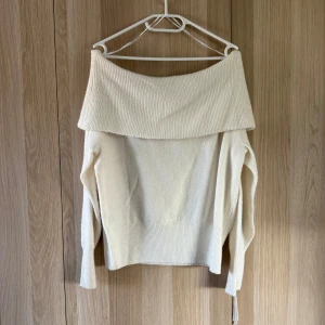 Offshoulder stickad tröja från H&M - Krämvit stickad tröja från H&M i offshoulder-modell med bred, ribbad krage. Långärmad och mjuk, perfekt för lager-på-lager under höst och vinter. Snygg och enkel att styla med jeans eller kjol.