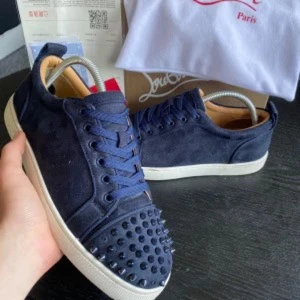 Marinblåa Louboutin sneakers med nitar - Snygga svarta sneakers från Christian Louboutin med ikoniska röda sulor och svarta nitar på tån. Skorna har snörning, rund tå och är tillverkade i mocka med läderdetaljer. Perfekt för dig som vill sticka ut med en edgy och lyxig stil.Allt og finns kvar 