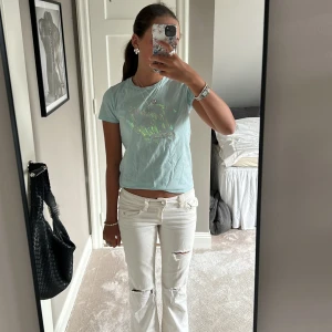 Ljusblå t-shirt från Tommy Hilfiger - Ljusblå t-shirt från Tommy Hilfiger med holografiskt tryck på bröstet och liten logga på ärmen. Modellen är kortärmad och har en klassisk rund hals. Materialet är mjuk bomull och passformen är normal. Perfekt för dig som gillar stilrena och coola detaljer.