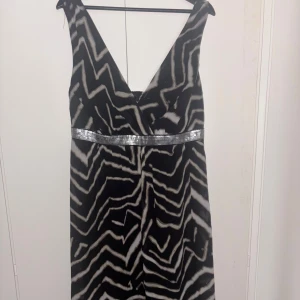 Långklänning  - Snygg svart långklänning med v-ringad hals och zebramönster i vitt och grått. Klänningen har en glittrig silverpaljett-detalj i midjan som ger extra edge. 