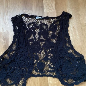 Svart spetsväst bohem hippie rave - Säljer en svart väst från Kaffe med vackert virkad spets och blommigt mönster. Västen är öppen framtill och har en bohemisk vibe, perfekt att slänga över en enkel topp för att lyfta outfiten.