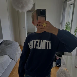 Mörkblå sweatshirt  - Mörkblå sweatshirt från Gina Tricot med stor vit ATHLETICA-text framtill. Klassisk rund hals, ribbade muddar och avslappnad passform. Mjuk insida i bomullsblandning. Perfekt för en sportig och avslappnad look!💙