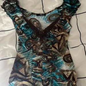 Vintage Y2K Turkos Brun topp Jane Norman - Unik blus med turkos och brunt mönster från Jane Norman. Toppen har v-ringning med broderade och pärlprydda detaljer samt rynkade, korta ärmar. Figurnära passform och stretchigt material som känns bekvämt och snyggt. Köpt på etsy ! 