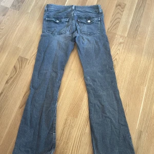 Blå bootcut jeans med fickdetaljer - Snygga blå jeans med bootcut passform och coola fickor med lock och knapp bak. Jeansen har klassisk femficksdesign och dubbla knappar i midjan. 