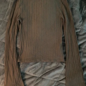 Brun ribbad långärmad tröja - Säljer en brun ribbad långärmad tröja med tight passform och utsvängda ärmar. Tröjan har en rund halsringning och är gjord i mjukt, stretchigt material som sitter snyggt på kroppen. Perfekt att styla med jeans eller kjol för en chill look. 