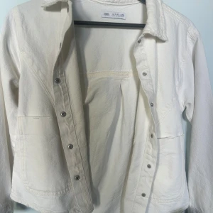 Vit jeansjacka från Zara  - Snygg vit jeansjacka från Zara i mjuk bomull. Jackan har klassisk krage, stora fickor framtill och knäppning med silvriga knappar. Perfekt att slänga över en hoodie eller t-shirt för en chill look.