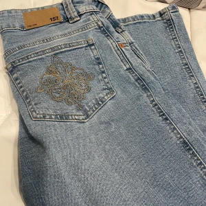 Ljusblå jeans med broderad ficka - Säljer ett par ljusblå jeans med snyggt broderi i guld på bakfickan. Storlek S Short Length. Använd 1 gång🥰