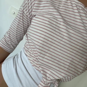 Randig rosa och vit tröja med knyt - Säljer en söt randig tröja i ljusrosa och vitt med trekvartsärm och knyt framtill i midjan. Jag brukar andvända med ett vitt linne under(såsom på bilderna).