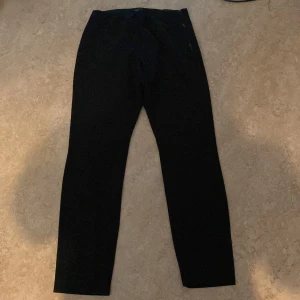 Svarta byxor med dragkedja - Svarta byxor med rak passform och diskret dragkedja i sidan. Snygg minimalistisk look som passar till det mesta. Materialet känns mjukt och stretchigt, perfekt för dig som gillar stilrena plagg med en twist.