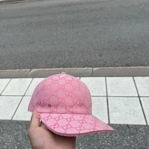 Rosa Gucci keps med GG-mönster - Snygg rosa keps från Gucci med ikoniskt GG-mönster över hela kepsen. Kepsen har böjd skärm och klassisk passform. Tillverkad i bomullsmix med vita detaljer på insidan och tydlig Gucci-tag. Perfekt för dig som vill sticka ut med en lyxig accessoar. Dustbag medföljer 