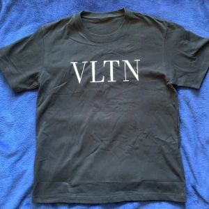 Svart VLTN t-shirt  Valentino - Svart t-shirt från Valentino med stor vit VLTN-logga på bröstet. Klassisk rund halsringning och korta ärmar. Tillverkad i mjuk bomull som känns skön mot huden. Perfekt för dig som gillar stilrena och trendiga plagg med tydlig logga. Helt ny skriv vid funderingar