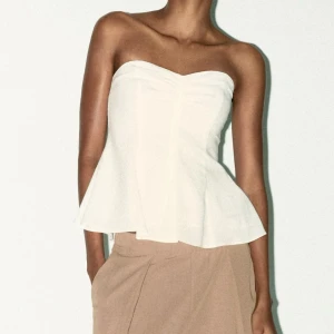 Vit linne tubtopp - Säljer en vit tubtopp i linne från Zara med lätt volang nertill. Toppen är axelbandslös och har en snygg rynkning framtill. Den har även en dragkedja på sidan. Säljer för att den är för liten för mig, den är helt oanvänd med prislappen kvar och slut på hemsidan. 💕