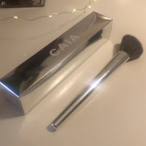 CAIA F06 sminkborste silver - Snygg CAIA F06 sminkborste med silvrigt handtag och mjuka, täta borst i mörkgrått. Perfekt för applicering av puder, bronzer eller rouge. Kommer i en stilren, spegelblank förpackning. Borsten är både lyxig och enkel att använda.