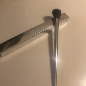 CAIA F23 sminkborste silver - Säljer en CAIA F23 sminkborste med silvrigt handtag och mjuka, täta borst i svart och grått. Perfekt för att applicera puder, rouge eller highlighter. Kommer i originalförpackning med stilren metallic finish.