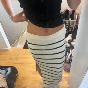 Randig stickad långkjol med slits - Säljer en snygg stickad långkjol i vitt med svarta horisontella ränder. Kjolen har en tight passform och en slits på sidan som ger en chill vibe. Perfekt för dig som gillar en enkel men trendig look.