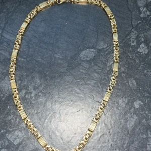 Guldfärgat kedjehalsband och armband - Säljer ett halsband i guldfärg. Halsbandet har en chunky kedjedesign med rektangulära, texturerade länkar och robusta karbinlås. Perfekt för dig som gillar statement-smycken med lite extra edge.