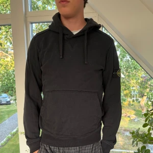 Stones Island hoodie Svart - Svart hoodie från Stone Island med klassisk patch på vänster ärm. Tröjan har huva med snörnin, perfekt för en chill och stilren look. Såklart äkta