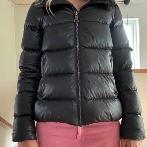 Mörkblå glansig Colmar pufferjacka med dragkedja - Säljer en mörkblå glansig pufferjacka från Colmar med klassisk logga på bröstet och nertill. Jackan har en hög krage, breda kanaler och dragkedja framtill. Perfekt för kalla dagar och riktigt snygg till streetwear-stilen.