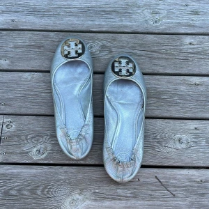 Silvriga ballerinaskor från Tory Burch - Snygga ballerinaskor i metallic-silver från Tory Burch med rund tå och stor logga i metall framtill. Skorna är gjorda i skinn med lätt struktur och har platt sula. Perfekta för dig som vill sticka ut med en glansig touch. 💕Köpte dessa på Sellpy och använde dem 1 gång på studentbalen☺️😇De är storlek 39 men små i storleken så passar även 38🤩