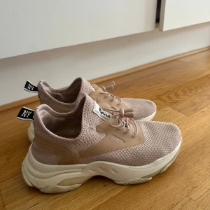 Beige sneakers från Steve Madden - Snygga beige sneakers från Steve Madden med stickad ovandel och chunky vit sula. Skorna har elastisk snörning med plastdetaljer och svart NY-detalj på hälen. Perfekta för en trendig och sportig look.