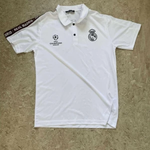 Real Madrid Champions League tröja 2st! 1st 299kr 2st 500kr - Snygg fotbollströja från Real Madrid med Champions League-logga och klubbmärke på bröstet. Finns i både vit och svart med kontrasterande tryck och texten 'REAL MADRID' på ena ärmen och ryggen. Klassisk pikékrage och korta ärmar. Tillverkad i lätt och ventilerande material.