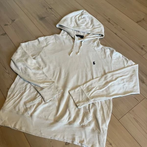 Vit hoodie från Polo Ralph Lauren - Snygg vit hoodie från Polo Ralph Lauren med klassisk broderad logga på bröstet. Tröjan har huva med snörning och en stor magficka. Tillverkad i mjuk bomull, perfekt för chill dagar. Långärmad och med relaxed fit. Den är i fint skick och allmänt stilig helt enkelt, passar väldigt bra nu i sommartider