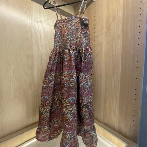Mönstrad långklänning - Färgglad mönstrad långklänning, köpt i Grekland, med smock upptill och tunna axelband. Klänningen har ett detaljerat blommigt och paisleyinspirerat färglagt mönster. Tillverkad i ett lätt tyg, perfekt för varma dagar. Står ingen Stl men skulle passa S och xs. Knappt använd. 