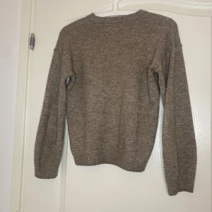 Beige stickad tröja från H&M - En enkel och stilren beige stickad tröja från H&M i storlek 134/140. Tröjan har rund halsringning, långa ärmar och ribbade muddar vid ärmslut och nederkant. Perfekt för lager-på-lager under kyliga dagar.
