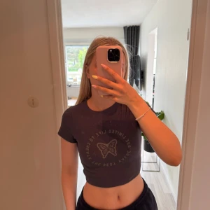 Mörkblå croppad topp med fjäril  - Säljer en mörkblå croppad topp med ribbad struktur och tryck av en fjäril samt text framtill. 