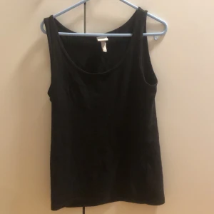 Svart linnetopp från H&M Basics - Enkel svart linnetopp från H&M Basics med rund halsringning och ärmlös design. Perfekt att matcha med jeans eller kjol. Tillverkad i mjuk bomull som känns skön mot huden. Snygg och stilren basic som funkar till allt.