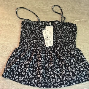 Blommig smockad linnetopp Gina Tricot - Supersöt smockad linnetopp från Gina Tricot med tunna axelband och blommigt mönster i vitt och ljusblått på mörkblå botten. Perfekt för varma dagar och enkel att styla med jeans eller kjol. Luftig och bekväm passform.