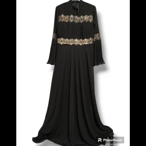 Långärmad Svart/guld festklänningar I Nyskick  - Festklänning med långa armar och mönsterdetaljer i  guld färg  Oanvänd  