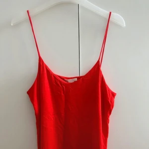 Röd linnetopp med tunna axelband - Enkel och snygg röd linnetopp med tunna axelband och rak passform. Perfekt för varma dagar och lätt att matcha med jeans eller kjol. Tidlös design som ger en fräsch look