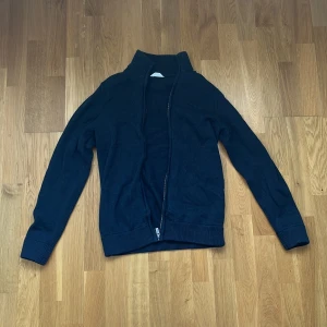 Mörkblå stickad kofta med dragkedja från Dobber  - Mysig mörkblå stickad kofta med hög krage och hel dragkedja framtill. Perfekt för lager-på-lager och enkel att matcha med olika outfits. Ribbstickade muddar vid ärmslut och nederkant ger en snygg och bekväm passform.