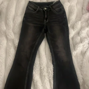 Svarta bootcut jeans med rå kant - Snygga svarta bootcut jeans med markerade vita sömmar och rå kant nertill. Jeansen har klassisk femficksmodell och dragkedja med knapp. Perfekta för dig som gillar en lite edgy stil och vill ha ett par jeans som sticker ut. Har sprättat upp byxorna nertill för att dom ska bli längre