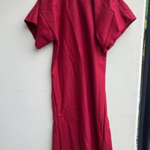 Röd långklänning i ylle - Enkel och stilren röd kjortel (historiskt herrplagg) i  ylle. Den har korta ärmar och v-ringad hals. Perfekt för dig som gillar klassiska och bekväma plagg med en tidlös känsla. Passar dig som vill sticka ut med en djup röd färg och naturligt material.  Röd kjortel. Ca L (dam) / M (herr) Det är alltså ett herrplagg men om man som kvinna vill porta en man från medeltiden så är dam-storlek med. Ca 105cm lång  Mäter vidd vid intresse då jag missade det!  Riktigt TUNN ylle.  Handfållad