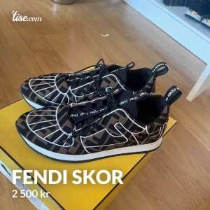 Fendi sneakers med logomönster - Snygga sneakers från Fendi med svart och brunt logomönster och vita detaljer. Skorna har snörning, rund tå och platt sula. Tillverkade i syntetmaterial och textil, med Fendi-logga på både snören och hälflik. Perfekta för dig som gillar statement sneakers.