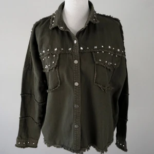 Grön jeansskjorta  - Grön jeansskjorta som även kan användas som overshirt med råa kanter och silvriga nitar på krage, bröstfickor och ärmslut. Overshirten har tryckknappar framtill, två stora bröstfickor och en loose passform. Funkar bra som jacka och shorts✨✨