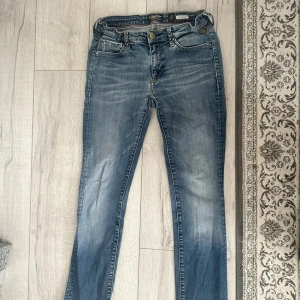 Blå Replay skinny jeans med slitningar - Snygga blå jeans från Replay med skinny fit och coola slitningar. Klassisk femficksmodell med detaljerade bakfickor och nitar vid fickorna fram. Jeansen har en något ljusare tvätt på låren och knäna för en trendig look.