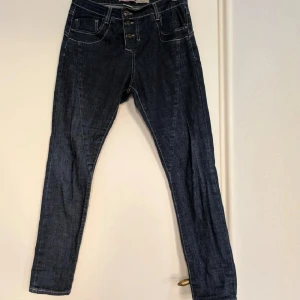 Mörkblå jeans från Please - Snygga mörkblå jeans från Please. Klassisk femficksmodell, dekorativa knappar framtill och coola detaljer som hjärta på bakfickan. Jeansen är i stretchigt denim och har kontrastsömmar för en trendig look. Bomull med stretch. 