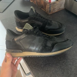 Valentino Rockrunner  - Snygga svarta Valentino Rockrunner sneakers med coola nitar på hälen och kamouflagemönster på sidorna. Skorna har snörning, platt sula och är tillverkade i en mix av skinn och mocka. Kontakta vid minsta fråga!