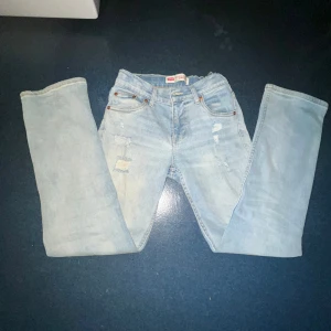 Levis 512 ljusa jeans med slitningar - Säljer ett par Levis 512 jeans i ljusblå denim med snygga slitningar och lagade detaljer framtill. Klassisk femficksmodell med raka ben och Levis-patch bak i midjan. Perfekta för en avslappnad och trendig look.