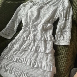 Vit spetsklänning med volanger bpc - Superfin vit kortklänning från Bonprix med spets över hela och flera rader volanger framtill. Klänningen har trekvartsärm och är fodrad med mjukt tyg under spetsen. Perfekt för dig som gillar romantisk och söt stil!