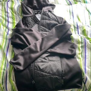 Svart quiltad jacka Only & Sons - Svart jacka från Only & Sons med quiltade partier och huva. Jackan har dragkedjor på sidorna och är tillverkad i syntetmaterial. Perfekt för dig som gillar en clean och sportig look. Passformen är normal och jackan har långa ärmar.