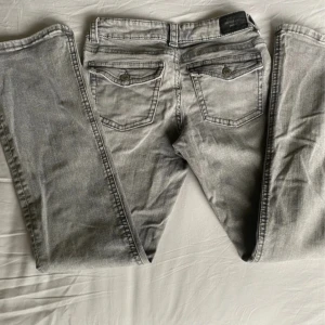 Grå jeans från Perfect Jeans - Snygga grå jeans från Gina tricot med klassisk femficksdesign och raka ben. Jeansen har en ljusgrå tvätt och detaljerade bakfickor med lock och knapp. Tillverkade i mjukt jeanstyg med dragkedjegylf och bälteshällor.