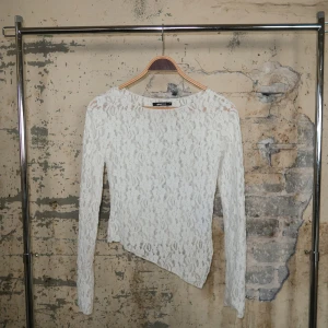 Vit spetsblus med asymmetrisk kant - Säljer en vit långärmad blus från Gina Tricot i genombruten spets med blommigt mönster. Toppen har en snygg asymmetrisk nederkant som ger en cool twist. Perfekt för dig som gillar romantiska detaljer och vill sticka ut lite extra.