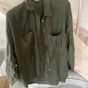 Olivgrön skjorta från Zara XS - Olivgrön skjorta från Zara i storlek XS. Skjortan har två stora bröstfickor, klassisk krage och knäppning framtill. Långärmad och i ett mjukt, lätt material som känns skönt mot huden. Perfekt för en avslappnad och cool look.