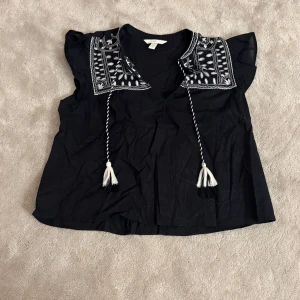 Svart blus - Svart blus från H&M med vita broderier på axlarna.